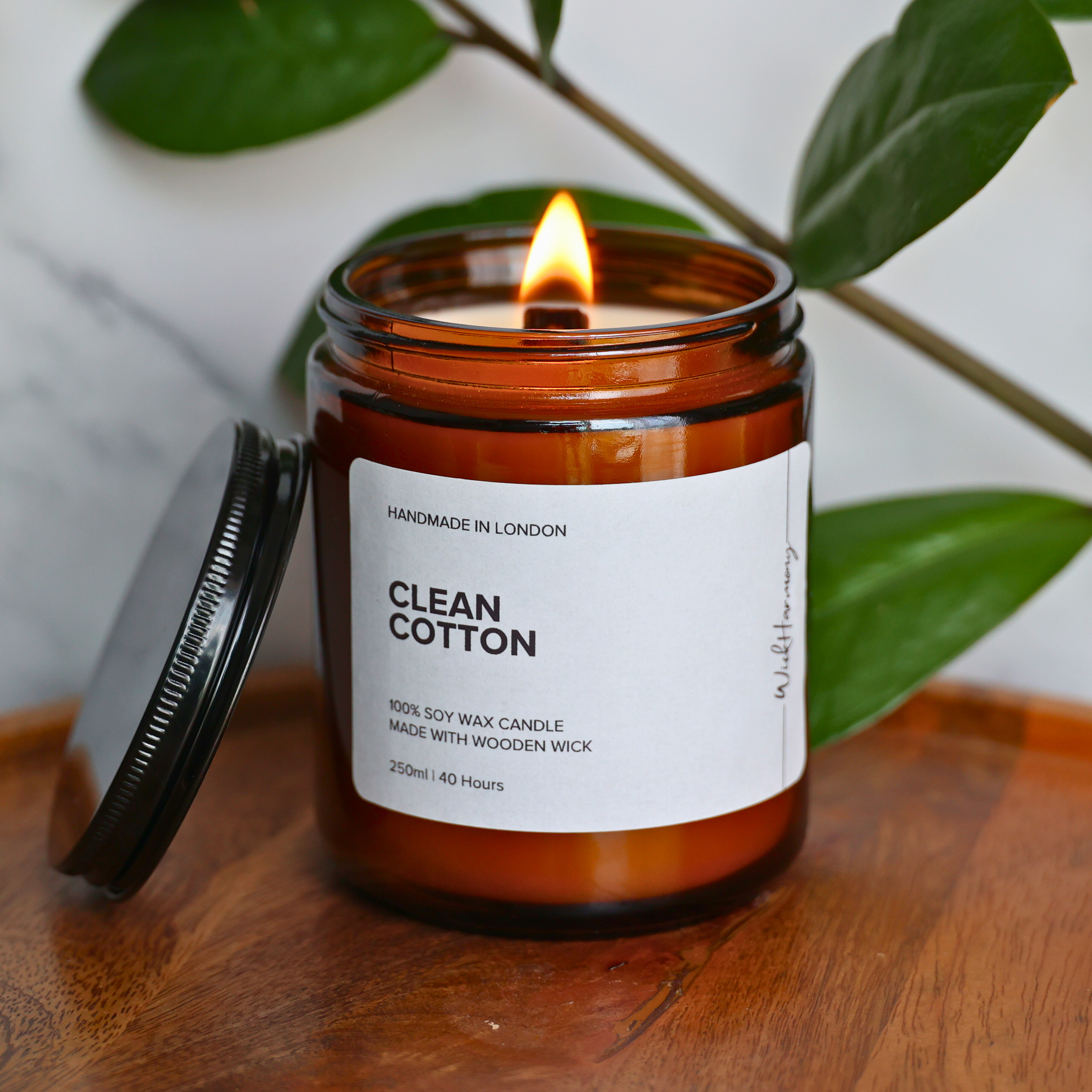 The 250ml 'Clean Cotton' wooden wick candle burning with a warm flame, creating a cozy ambiance on a wooden tray.