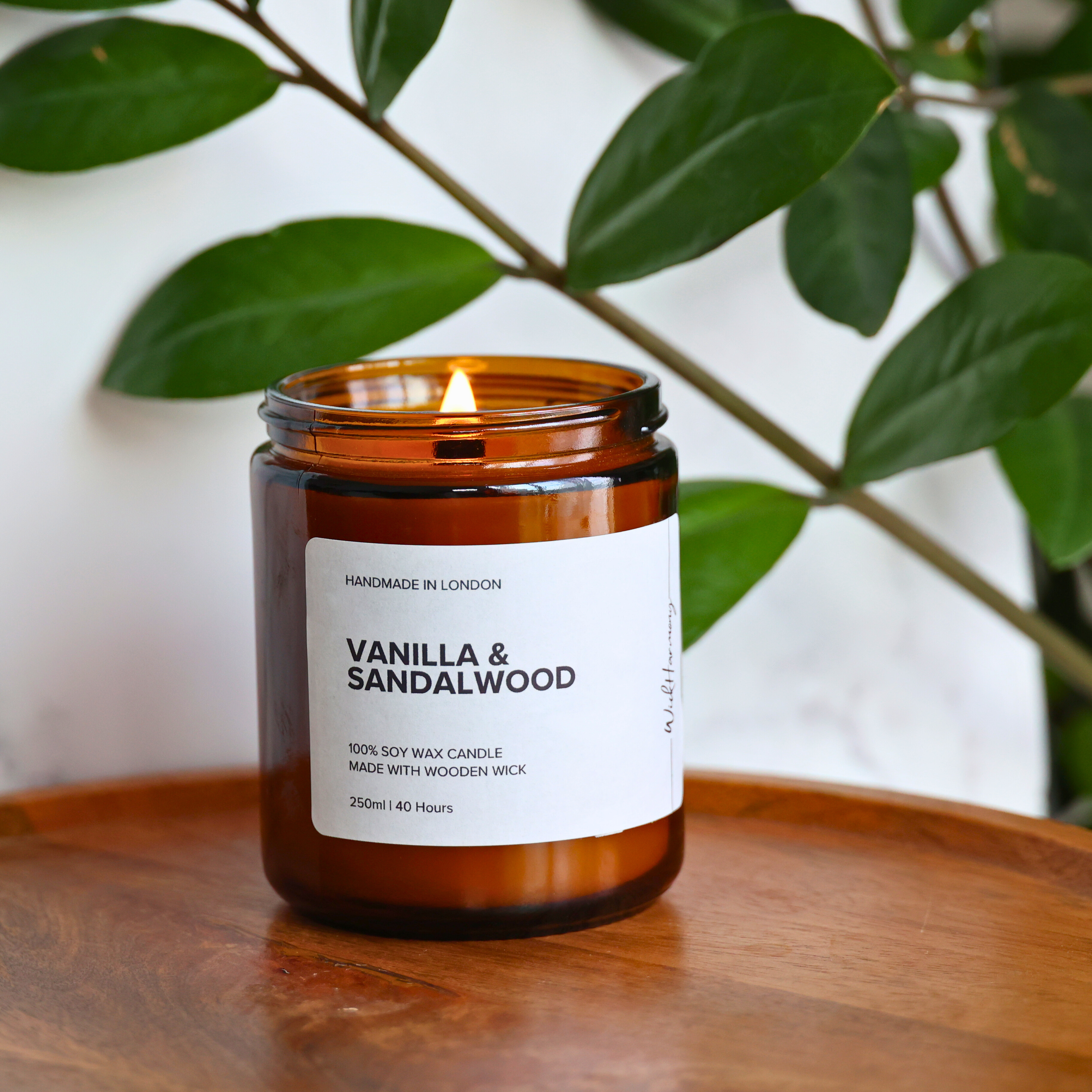The 250ml 'Vanilla & Sandalwood' wooden wick candle burning with a warm flame, shown in a cozy lifestyle setting.