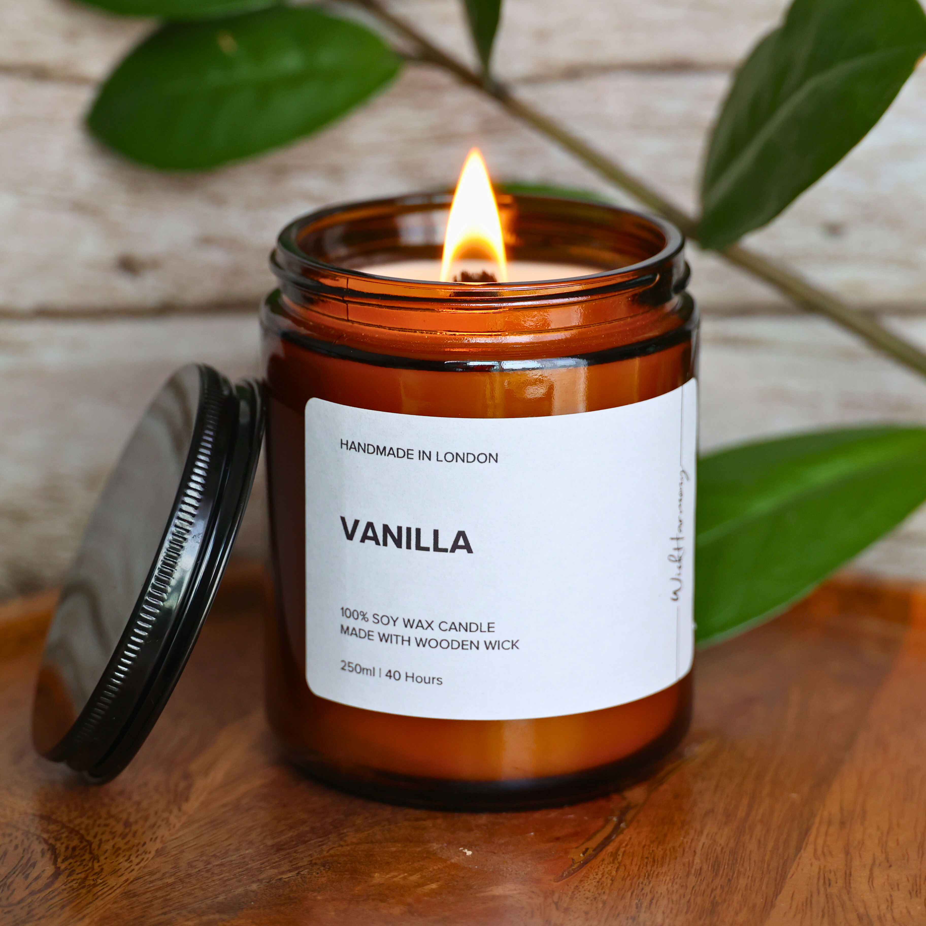 The 250ml 'Vanilla' wooden wick candle burning with a bright flame, creating a cozy scene on a wooden tray with the lid off.