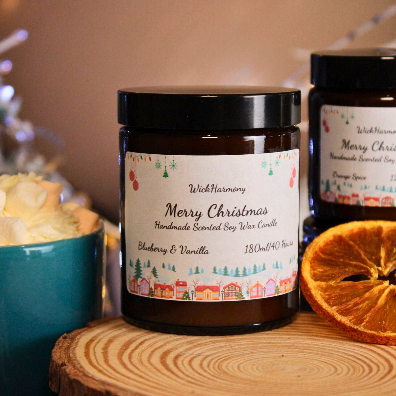 A festive display of different sized Christmas village candles with a dried orange slice and a mug of hot chocolate.