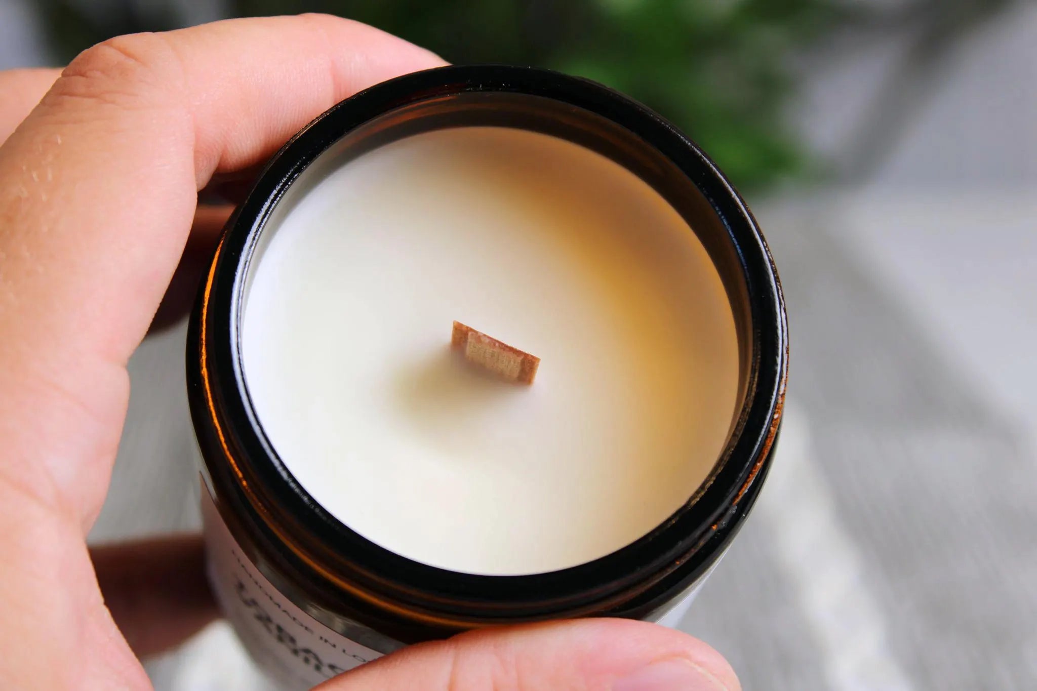 A close-up macro shot of a natural wooden wick set in smooth, creamy 100% soy wax