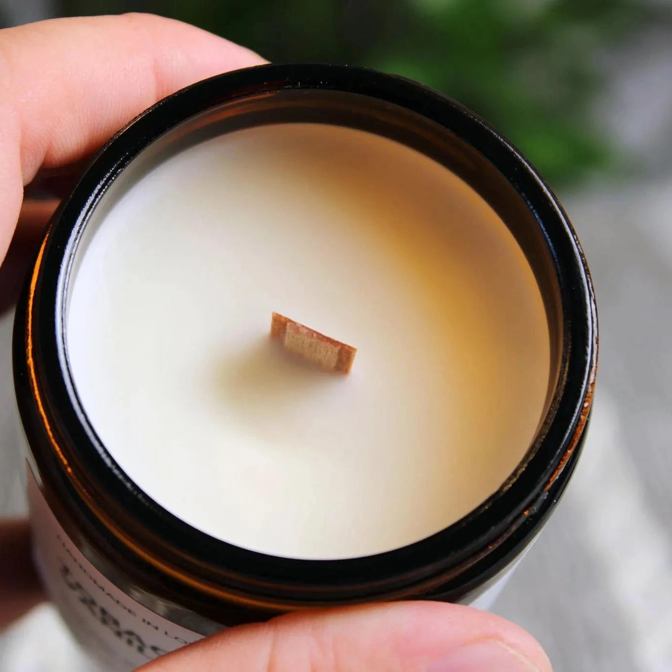 A close-up top-down view of a natural soy wax candle showing the wooden wick in an amber glass jar