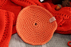 A handmade orange crochet candle coaster, styled with a cosy red jumper, providing a heat-resistant surface for candles.