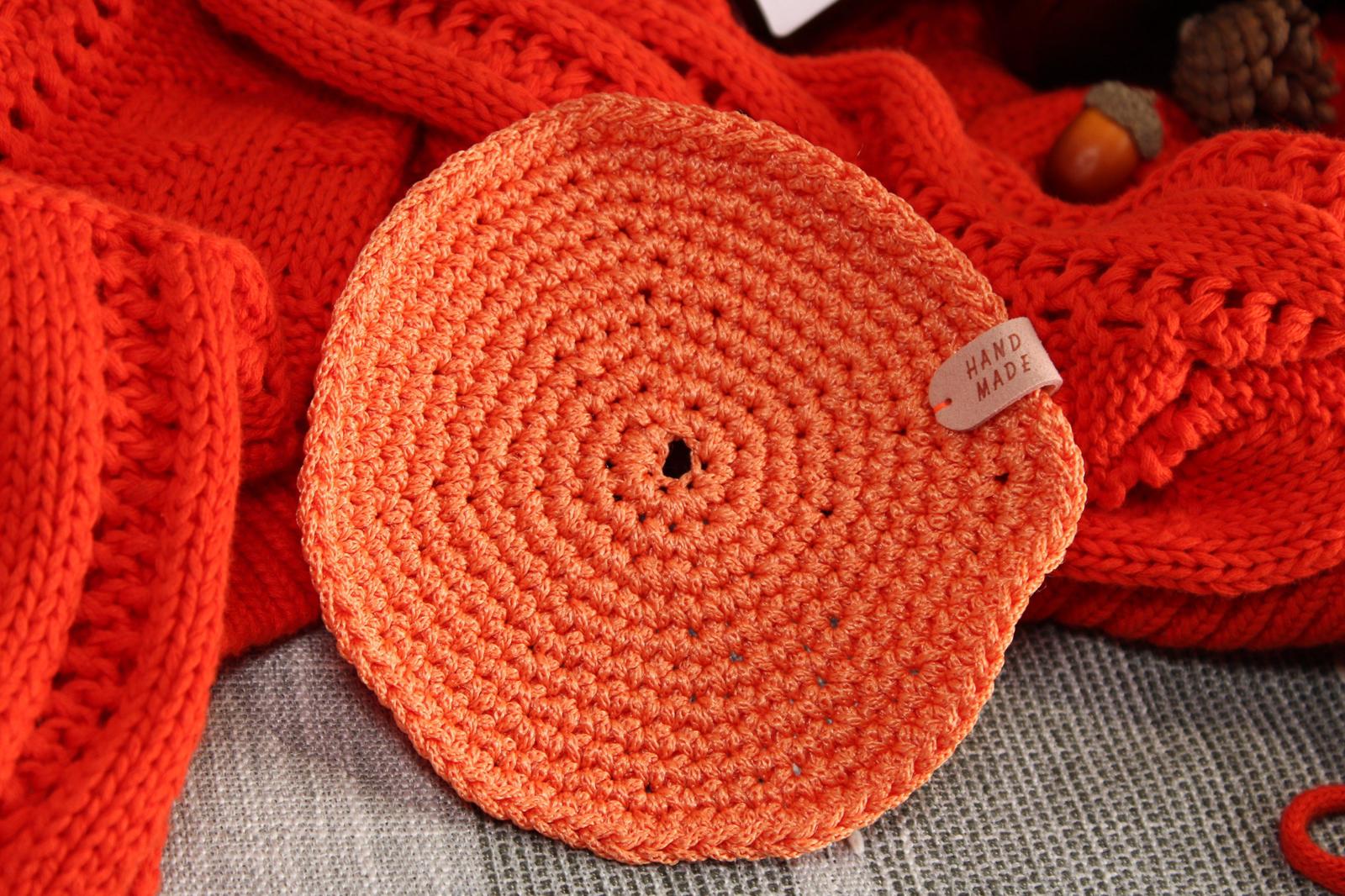 A handmade orange crochet candle coaster, styled with a cosy red jumper, providing a heat-resistant surface for candles.