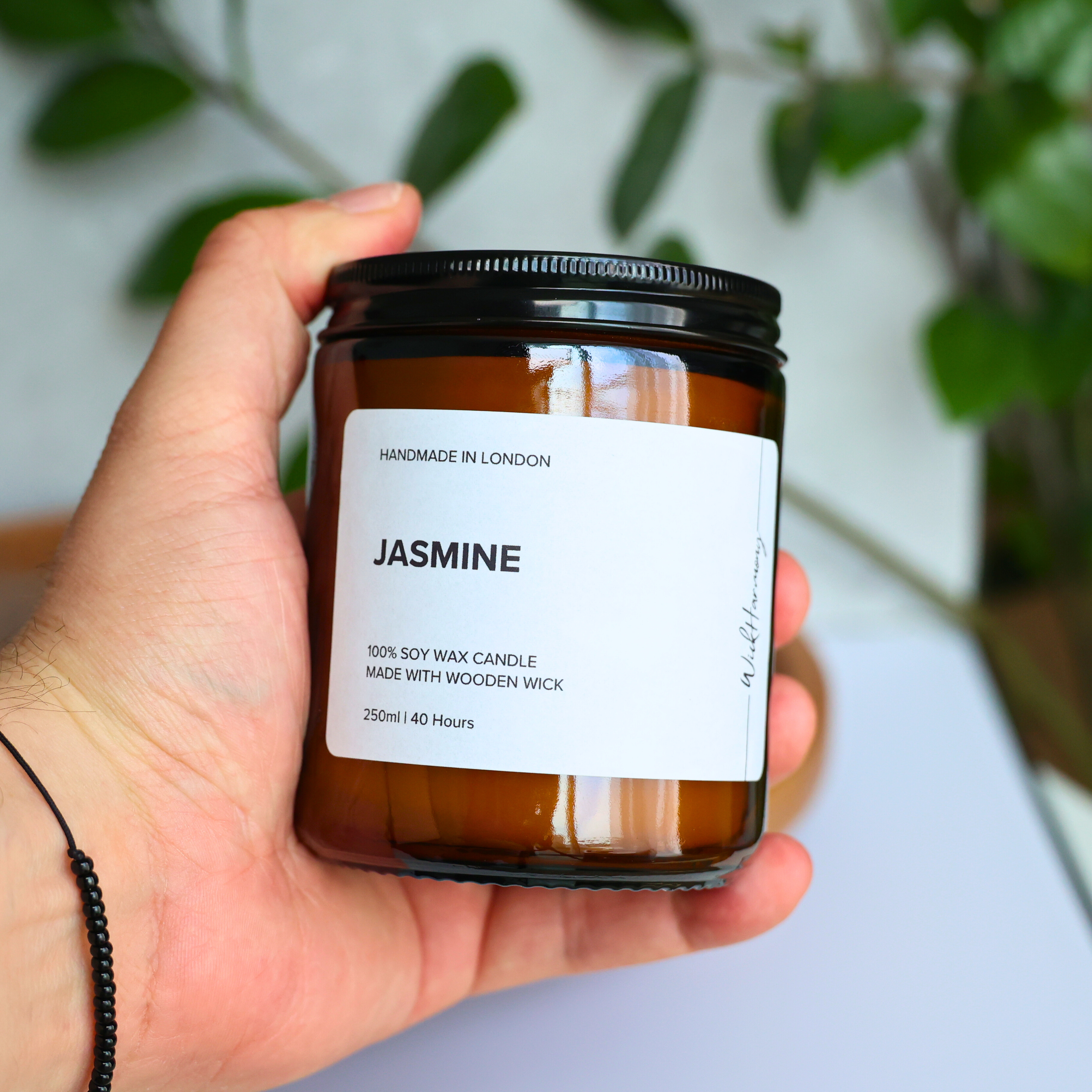 A hand holding the 250ml amber jar 'Jasmine' soy wax candle by WickHarmony to show its size and scale.