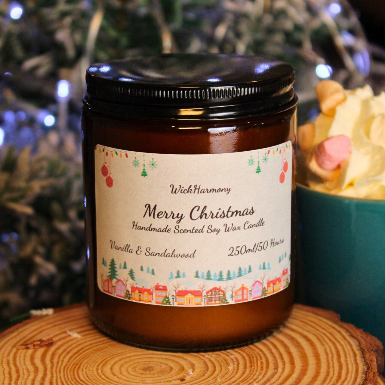 A large 250ml soy candle with a festive Christmas village label, sitting next to a mug of hot chocolate with whipped cream.