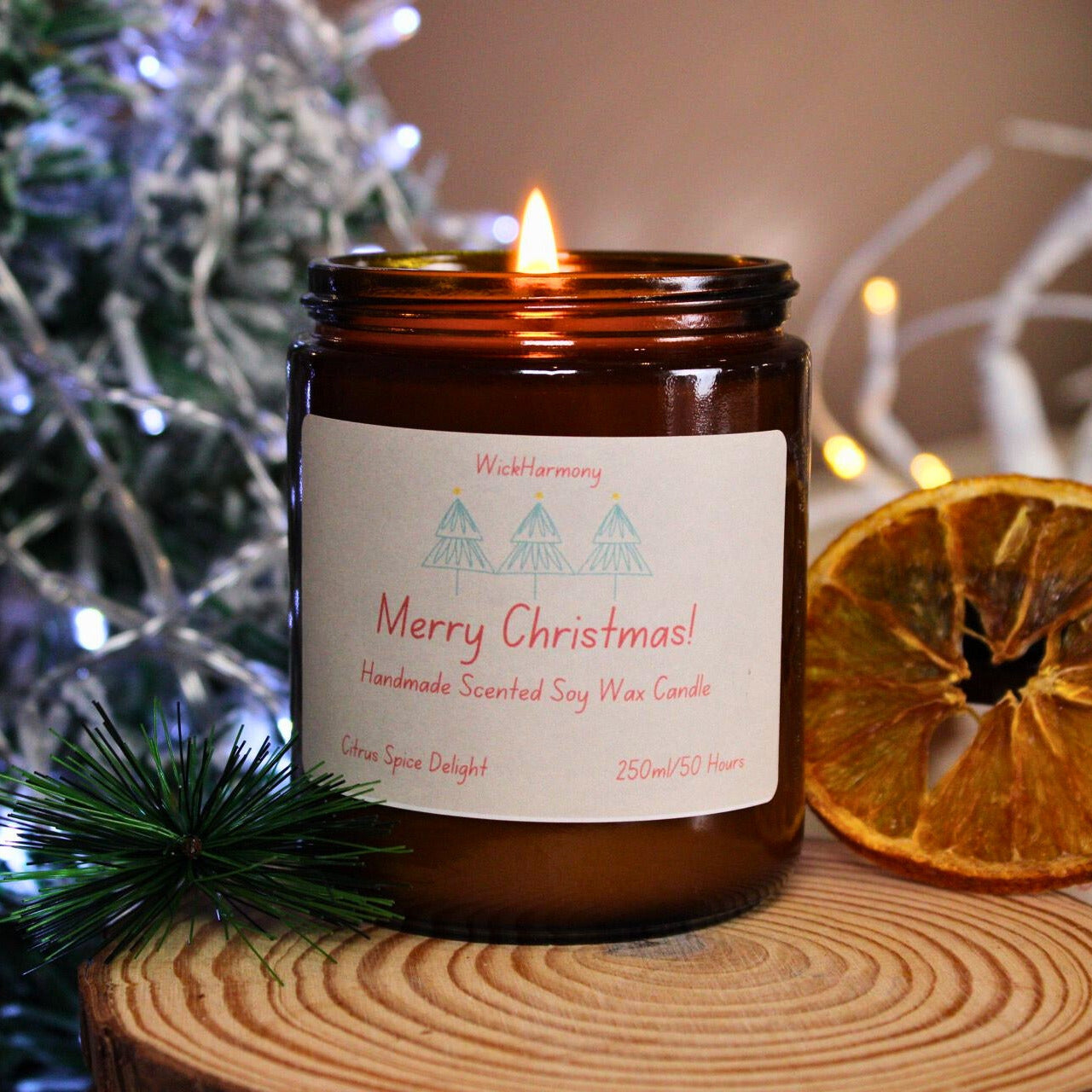 A large 250ml Christmas soy candle with a lit flame, featuring a minimalist three-tree design, sitting on a wood slice with a dried orange.