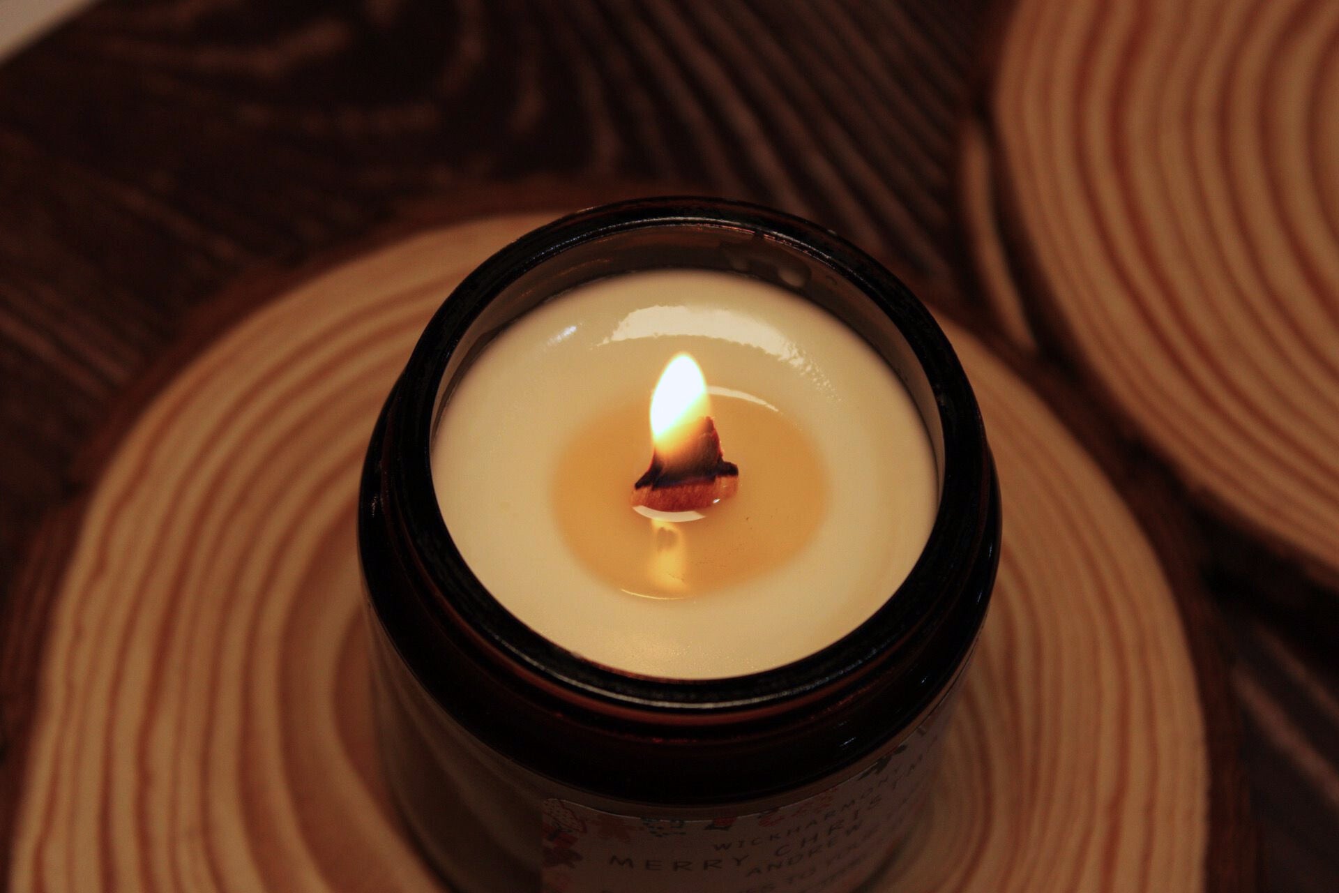 A top-down view of a lit crackling wood wick candle, showing a melted pool of soy wax and a warm, cosy flame.