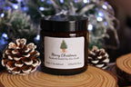 A medium 120ml Amber & Sandalwood scented Christmas candle with a personalised tree label, flanked by two pinecones.