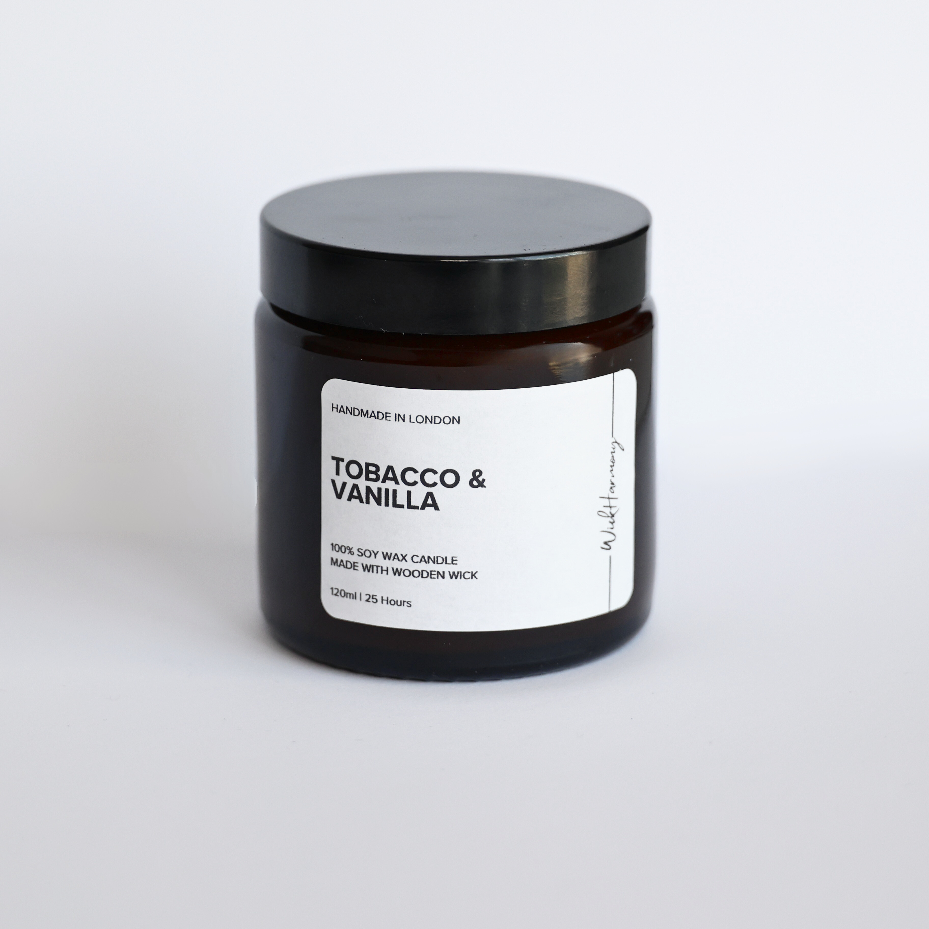 A studio product photo of the 120ml 'Tobacco & Vanilla' soy wax candle by WickHarmony, in an amber jar with a black lid.